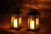 Two lit lanterns on a sandy surface with a warm glow.